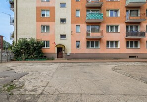En flervåningsbyggnad med bostäder, en central entré, balkonger och en plattlagd markyta.
