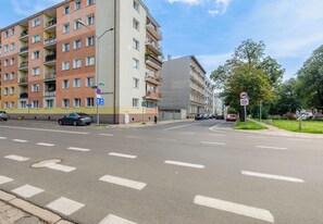 Ein mehrgeschossiges Wohngebäude mit Balkonen, eine Straße mit Zebrastreifen und ein Verbotsschild für Parkplätze.