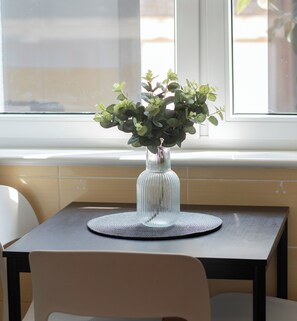 En tydlig bild av ett bord med en vas som innehåller gröna blad, placerad nära ett fönster med utsikt över omgivningen.