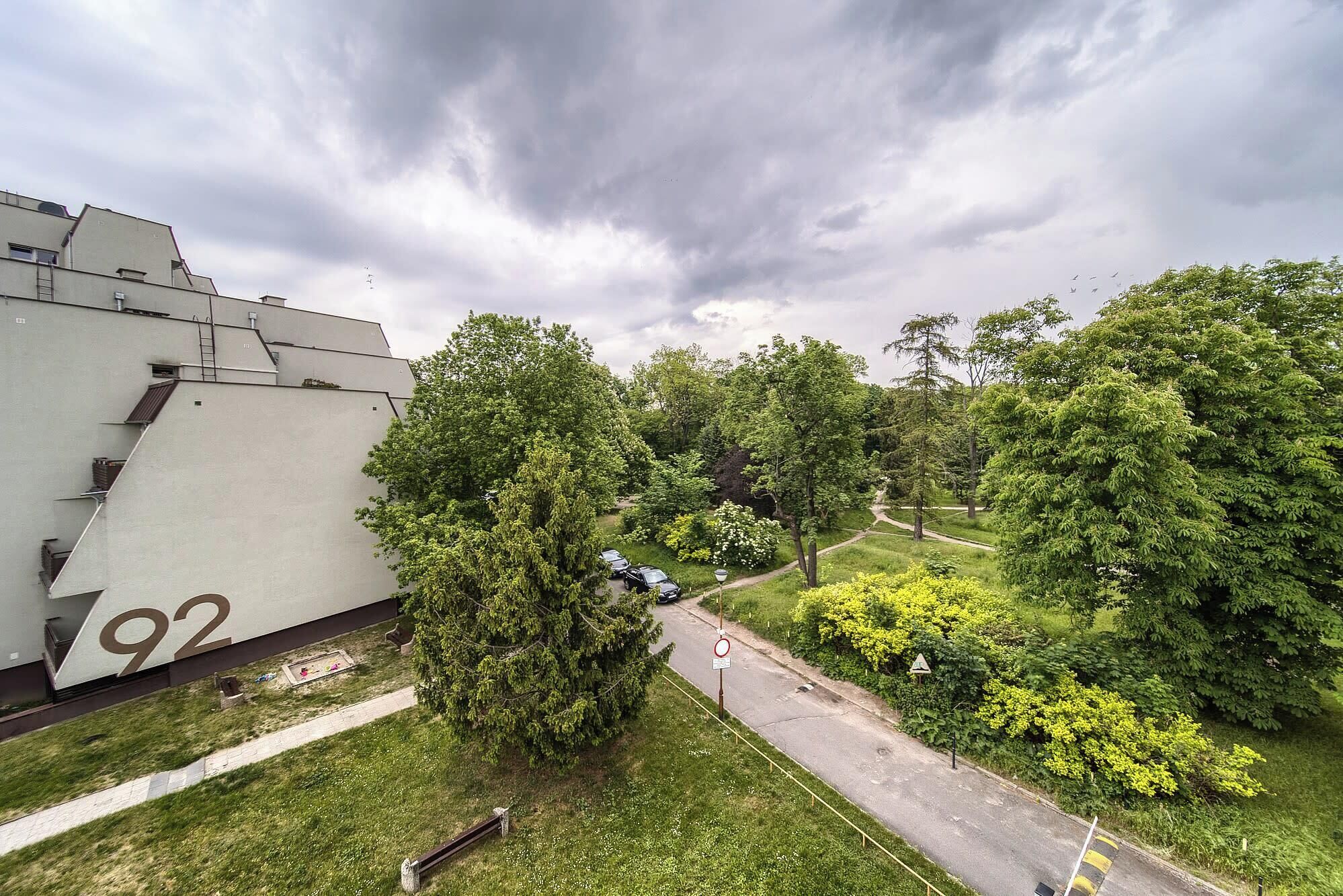 A residential area with a large building marked with the number 92, surrounded by lush greenery and a pathway.