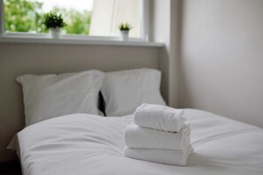 A neatly made bed with white linens and a stack of folded towels. - Park Skowroni Homely Studio (Wrocław)