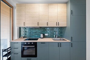 A modern kitchen with light wood cabinets, a stainless steel sink, and a built-in oven. - Jasna City Center Apartment (Lublin)