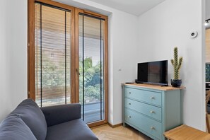 Ein Wohnzimmer mit einer Couch, einem Fernseher auf einer Kommode und einer Kakteenpflanze.