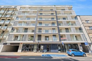 Ein mehrstöckiges Hotel mit Balkonen, einem Eingangsbereich im Erdgeschoss und einem Parkplatz.