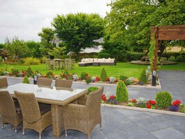 Un patio al aire libre con una mesa y sillas para comer, rodeado de un jardín con diversas plantas y flores.