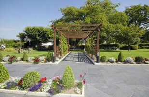 Un jardín con un pórtico de madera, senderos empedrados y diversos macizos de flores.