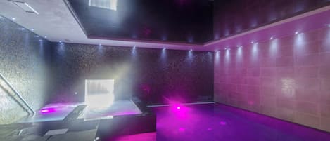 A modern spa room with a large bathtub, a massage table, and a wall with a textured pattern.