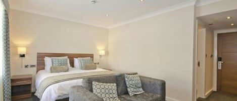 A hotel room with a bed, a grey sofa, and two wall-mounted lamps.