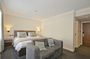 Una habitación de hotel con una cama, un sofá gris y dos lámparas de pared.