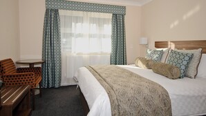 Habitación de hotel con cama, escritorio, silla y ventana con cortinas.