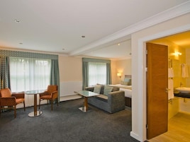 Habitación de hotel con comedor, sofá, una mesita y baño visible a través de una puerta abierta.