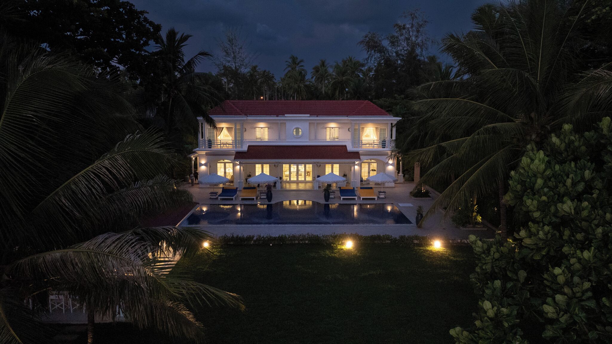 A large house with a swimming pool, surrounded by palm trees.