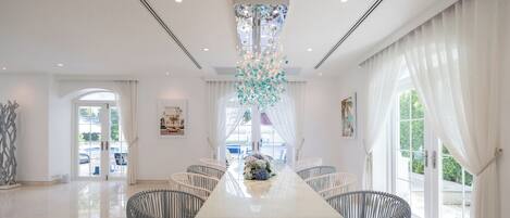 Un comedor amplio con una mesa larga, sillas blancas y una lámpara decorativa.