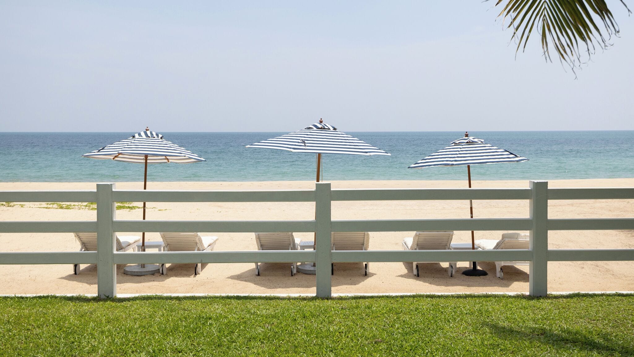 A beach view with three striped umbrellas and lounge chairs.