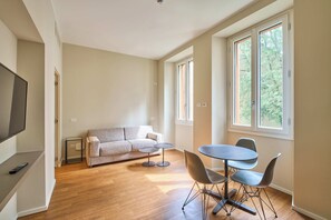 Ein Wohnzimmer mit einer Couch, einem Fernseher, einem Couchtisch und einem Esstisch mit Stühlen.