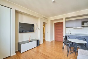 Eine moderne Küche mit Einbauofen, ein Essbereich mit rundem Tisch und Stühlen sowie ein an der Wand befestigter Fernseher.