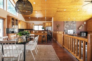 Una cocina amplia con armarios de madera, un comedor con sillas blancas y una pared de acento de piedra.