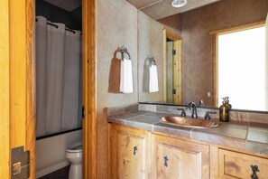 Un baño con tocador de madera, un lavamanos, un espejo y una cortina de ducha.