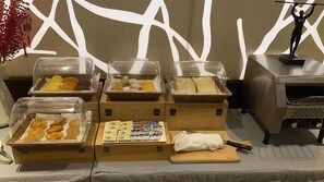 Montaje de bufé con diversos alimentos en recipientes cubiertos, una tabla de cortar con un cuchillo y una figura decorativa sobre un pedestal.