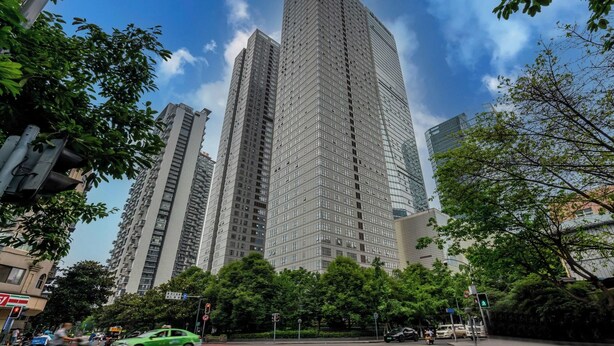 Un immeuble de grande hauteur  à l’architecture moderne, entouré d’arbres et d’autres bâtiments.