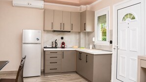 A compact kitchen with a refrigerator, a coffee maker, and a window with a view of greenery. - Dionysos Hotel (Kassandra)