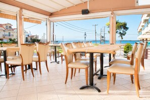 An outdoor dining area with tables and chairs, overlooking a body of water and buildings. - Dionysos Hotel (Kassandra)
