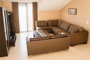 A living room with a sectional sofa, a glass coffee table, and a dark-colored entertainment unit. - Dionysos Hotel (Kassandra)