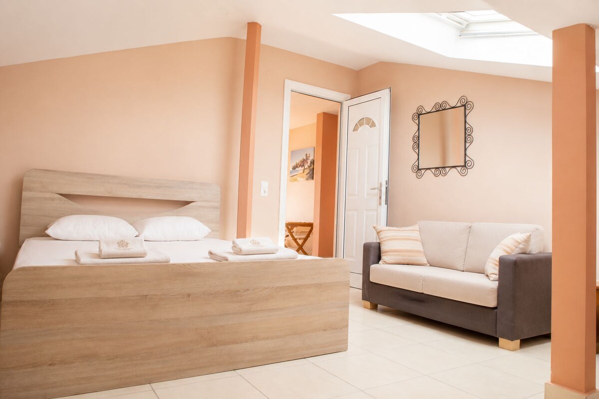 A bedroom with a bed, a sofa, a mirror, and a door leading to another room.