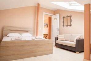 A bedroom with a bed, a sofa, a mirror, and a door leading to another room. - Dionysos Hotel (Kassandra)