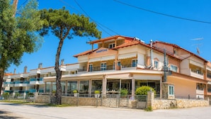 A multi-story hotel with balconies, a covered outdoor area, and a stone wall. - Dionysos Hotel (Kassandra)