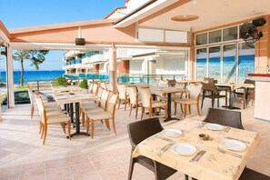 Restaurante con terraza al aire libre y vistas al mar, con varias mesas y sillas para comer.