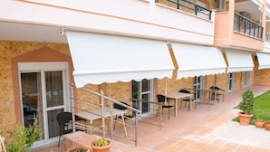 An outdoor patio area with a covered seating area, potted plants, and a staircase leading to an upper level. - Dionysos Hotel (Kassandra)