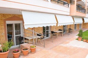 Un patio exterior con una zona de estar cubierta, plantas en macetas y una escalera que conduce a un nivel superior.