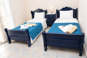 A hotel room with two single beds, each with a blue bedspread and white pillows, and a small bedside table with a lamp. - Dionysos Hotel (Kassandra)