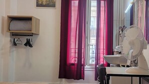 A room with a bed, a chair, a table, a fan, and a window with curtains. - Hotel Residence Saint Ouen (Saint-Ouen)