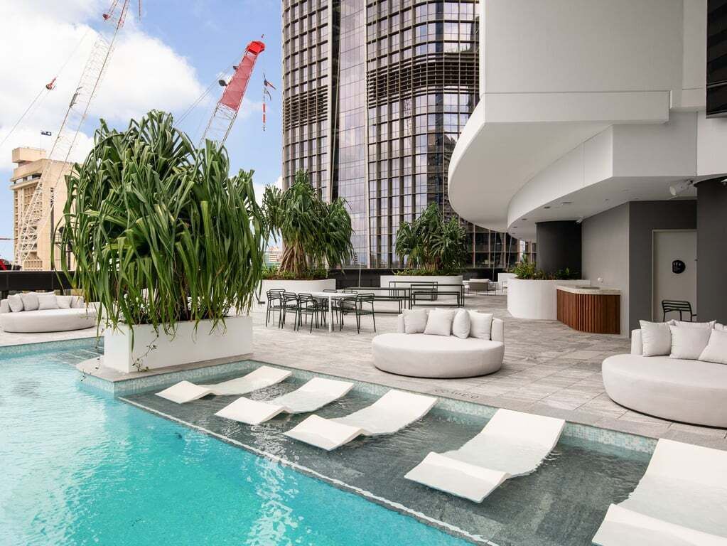 Un espace piscine aménagé sur le toit, avec des chaises longues, un coin repas et une vue sur les grands immeubles.