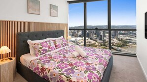A bedroom with a bed, a ceiling fan, a nightstand, and a large window with a city view. - Gorgeous Wide View 2BR High Level /Sunset/Casino (Brisbane)