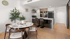 A modern kitchen with a central island, white cabinetry, and a dining area with a round table and chairs. - Gorgeous Wide View 2BR High Level /Sunset/Casino (Brisbane)