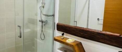 A bathroom with a glass shower enclosure, a toilet, a sink with a wooden countertop, and a mirror with a wooden frame.