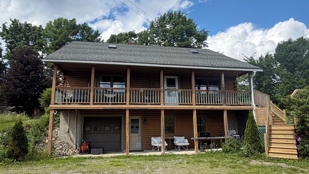 Een houten chalet van twee verdiepingen met balkon, garage en terras.