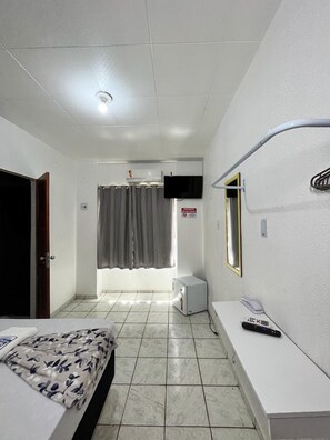 A hotel room with a bed, a desk, a chair, a television, and a bathroom with a shower curtain. - Hotel Avenida (Belém)