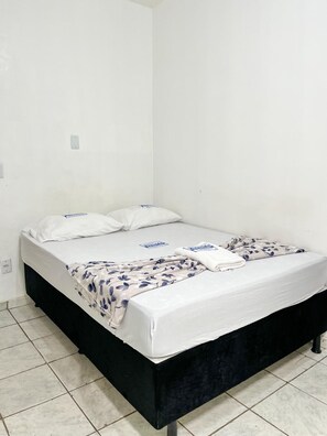 A single bed with a white mattress and black frame, a floral-patterned blanket, and two pillows. - Hotel Avenida (Belém)