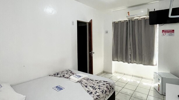 Quarto de hotel com cama, escrivaninha, cadeira, janela com cortinas e porta.