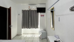 Quarto de hotel com cama, escrivaninha, cadeira, televisão e banheiro com cortina de chuveiro.