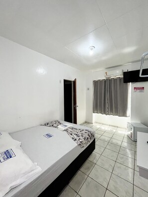 Habitación de hotel con cama, escritorio, silla, ventana con cortinas y puerta.