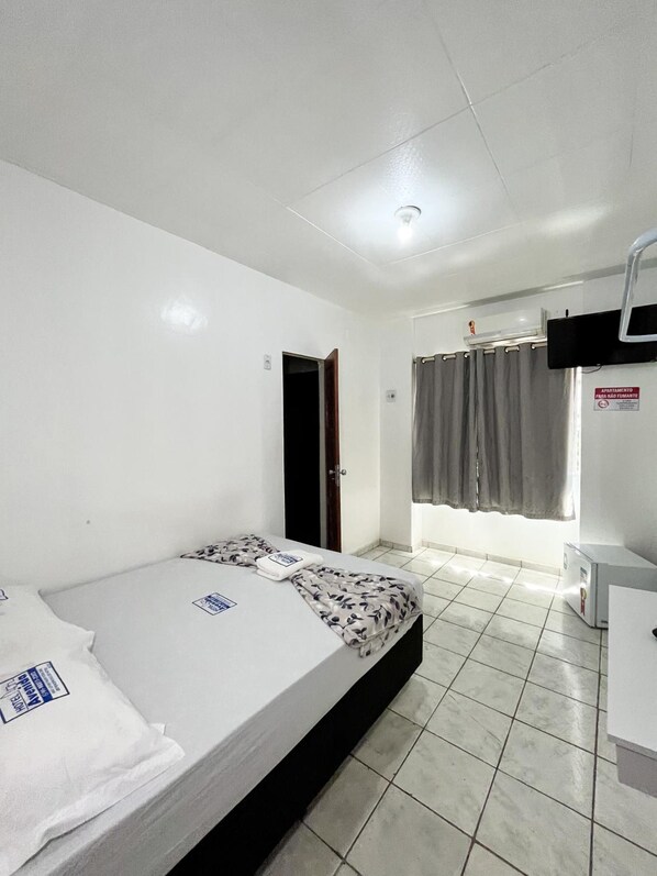 A hotel room with a bed, a desk, a chair, a window with curtains, and a door. - Hotel Avenida (Belém)
