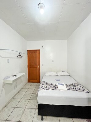 A small, clean room with a bed, a wooden door, and a white shelf. - Hotel Avenida (Belém)