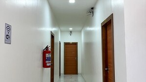 Um corredor com paredes brancas, um extintor de incêndio e uma porta no final.