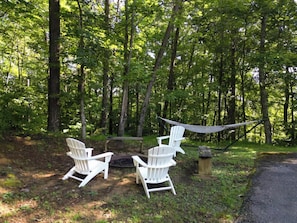 Et skovområde med to hvide Adirondack-stole og en hængekøje.