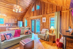 Ein gemütliches Cabin-Interieur mit Holzboden, einer Küchenzeile, einem Wohnzimmer mit Sofa und Sesseln und Blick ins Freie.